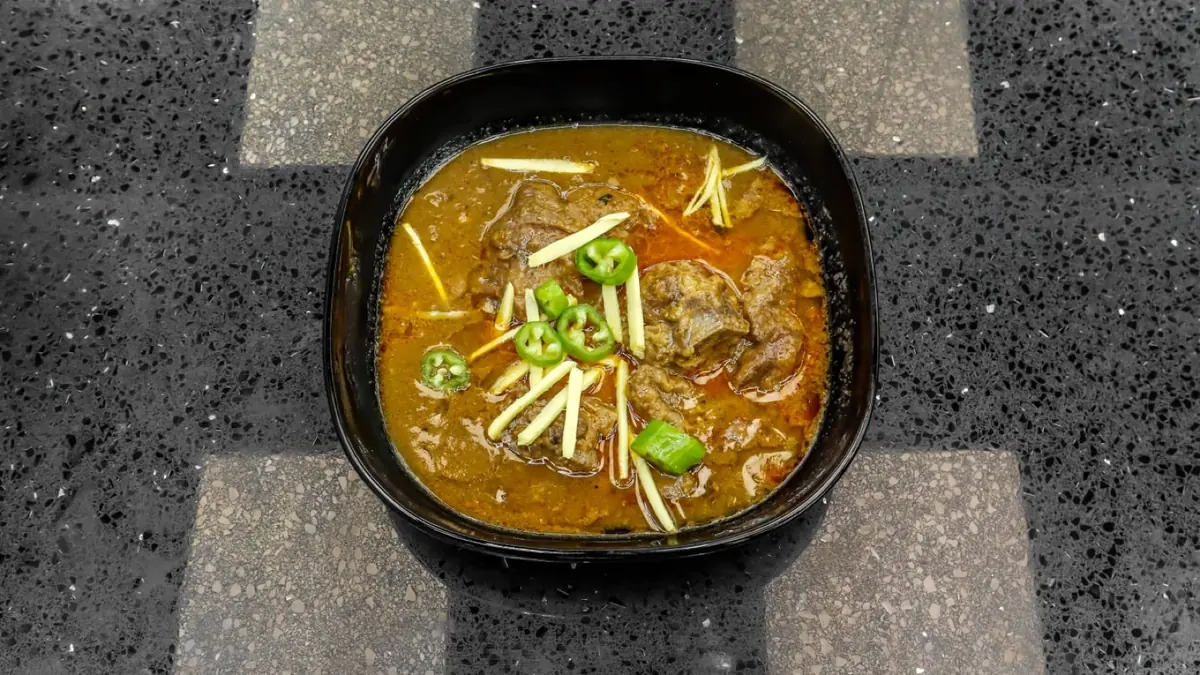 An overhead square detail of nihari with ginger and coriander on a grey terrazzo surface
