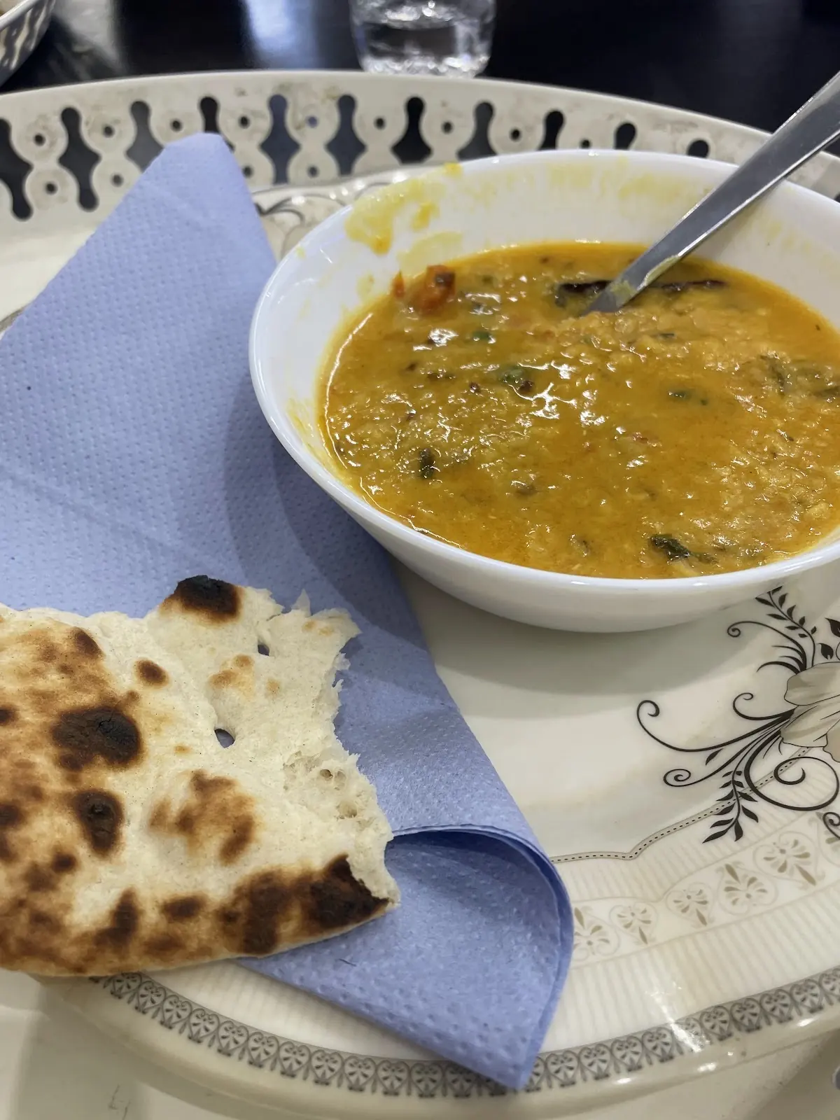 A restaurant table laid with haleem, naan and a blue napkin
